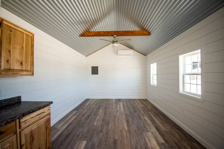 Outpost cabin interior with vaulted ceiling, wooden beams, and light wood cabinets.