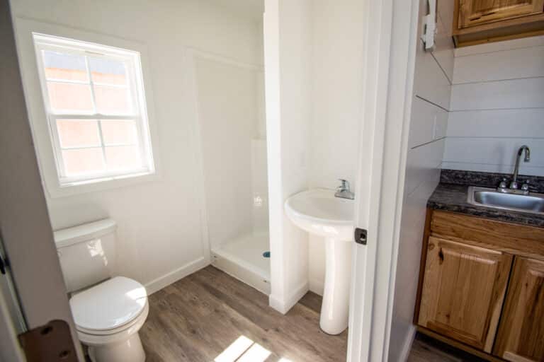 Small bathroom inside an Outpost cabin with a white toilet, pedestal sink, and natural wood vanity.